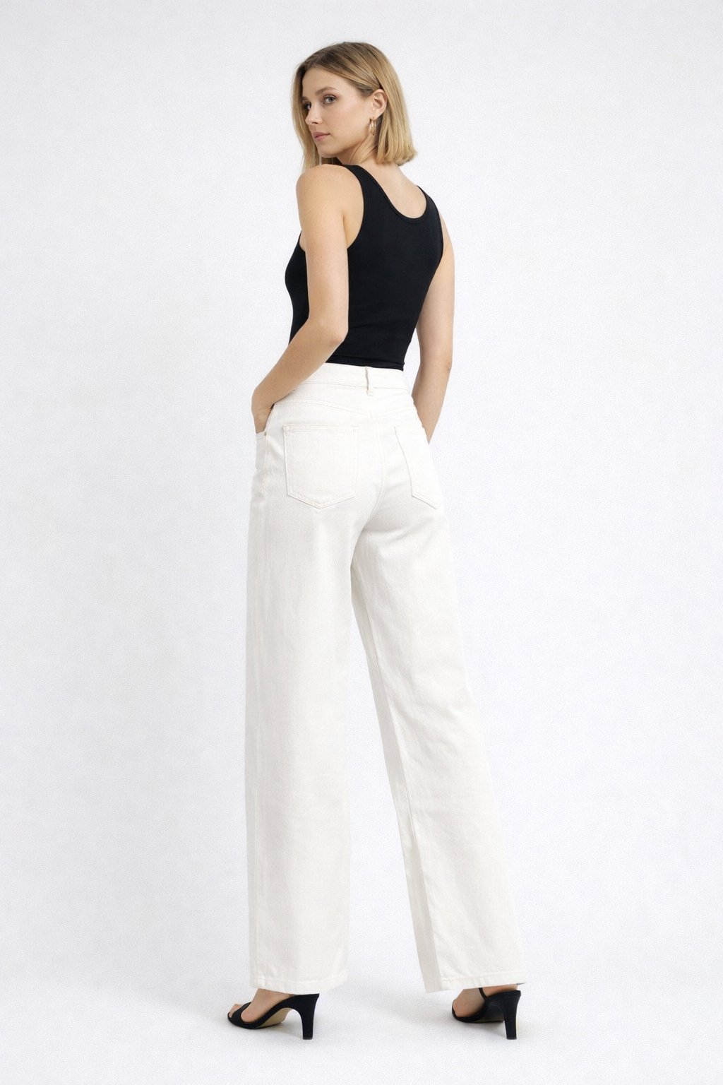 Woman wearing a black sleeveless top and white pants on a white background