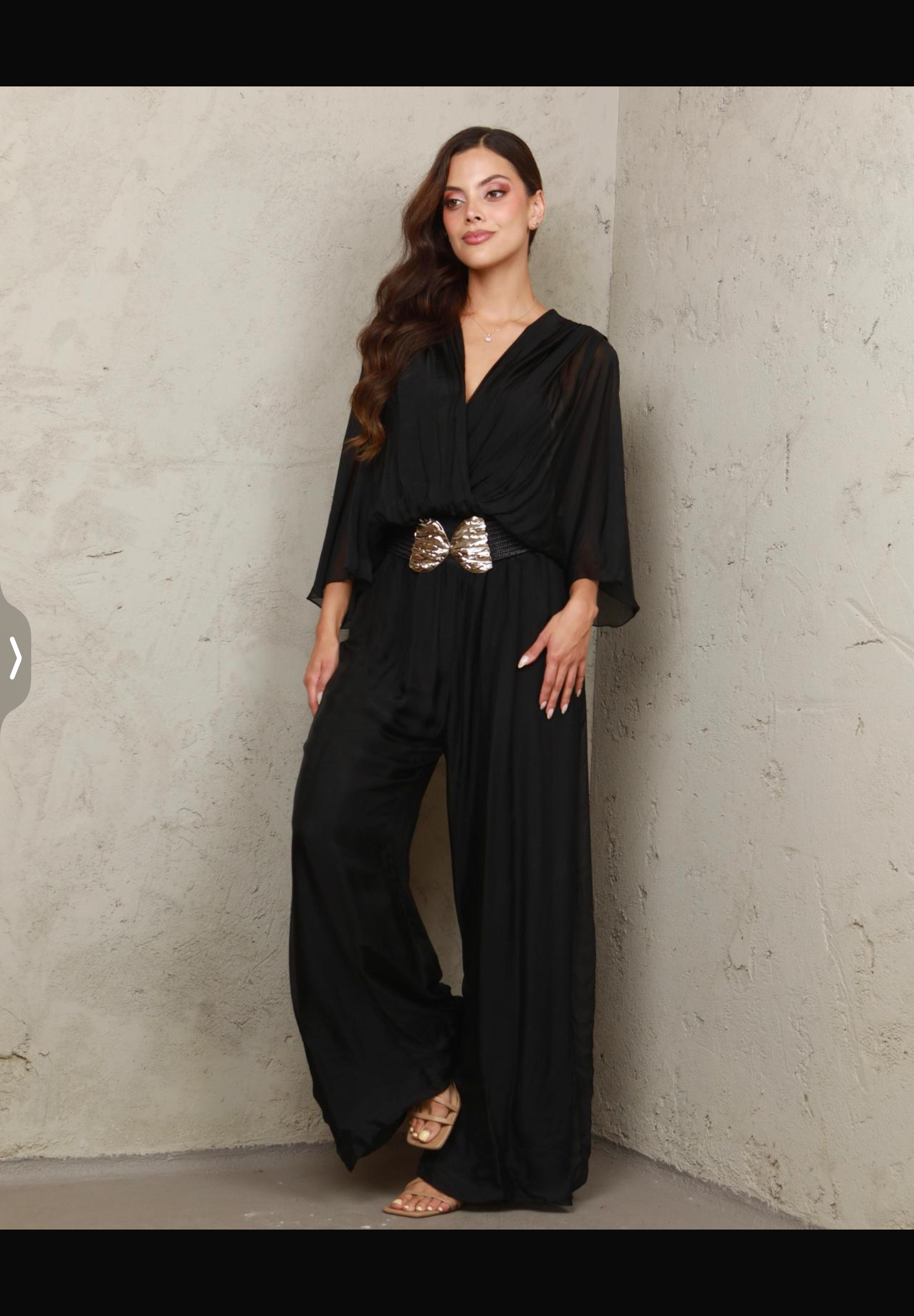 Woman wearing a black outfit with a belt against a plain wall