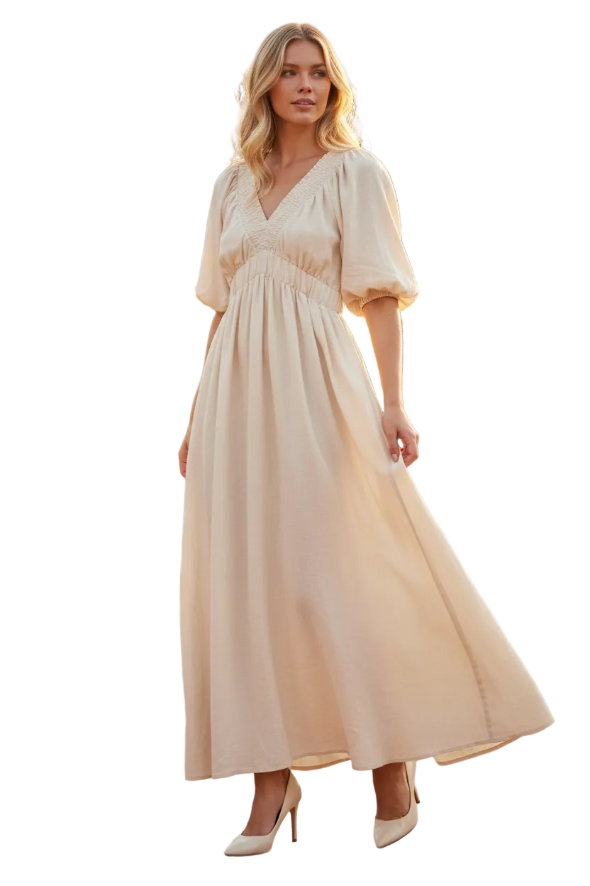 Woman wearing a beige dress standing outdoors with greenery in the background