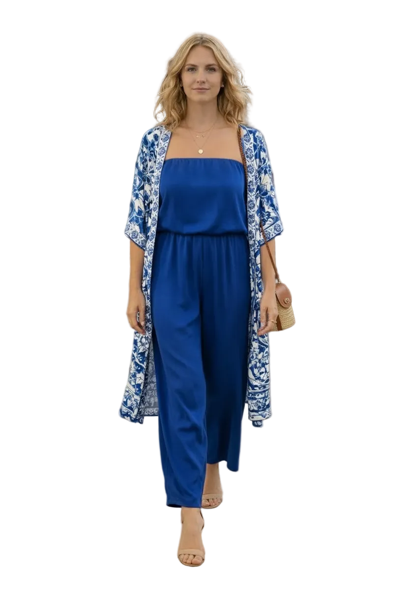 Woman in a blue dress and floral kimono standing in an outdoor setting with tables and people in the background.