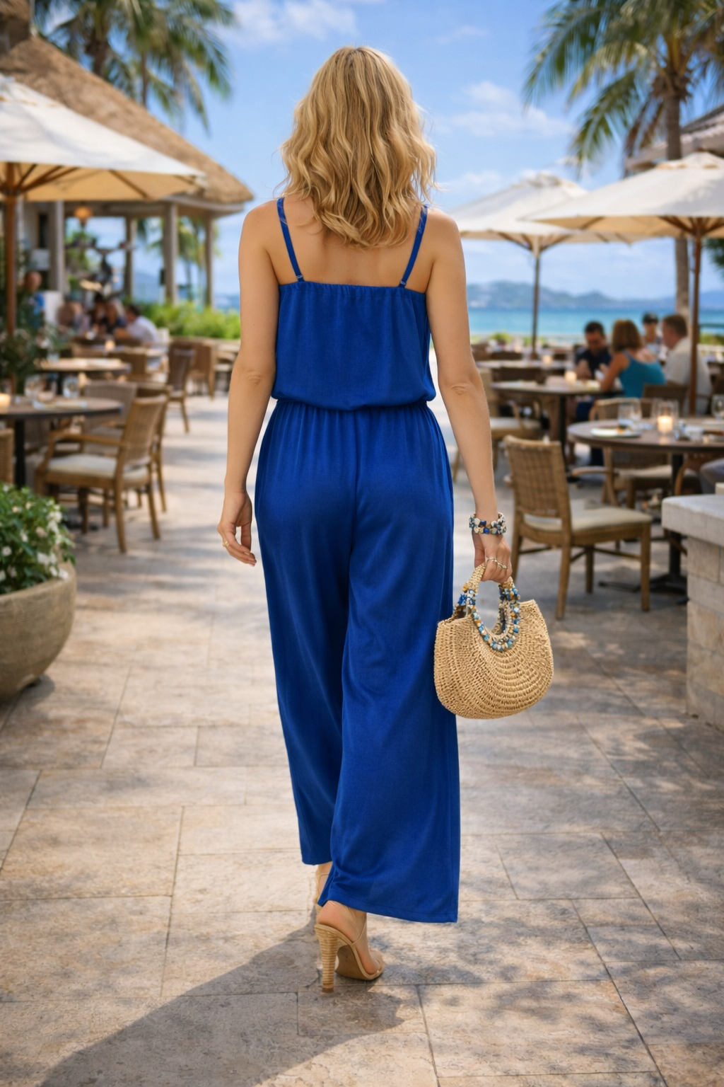 Woman in a blue jumpsuit walking outdoors with tables and chairs in the background